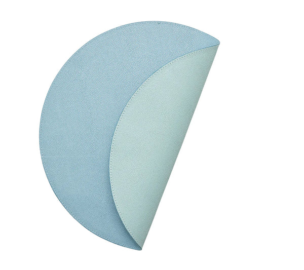 The Kim Seybert Icons Placemat Set of 4 features round, textured blue reversible placemats; each one curves to show a lighter blue underside and subtle shagreen texture.