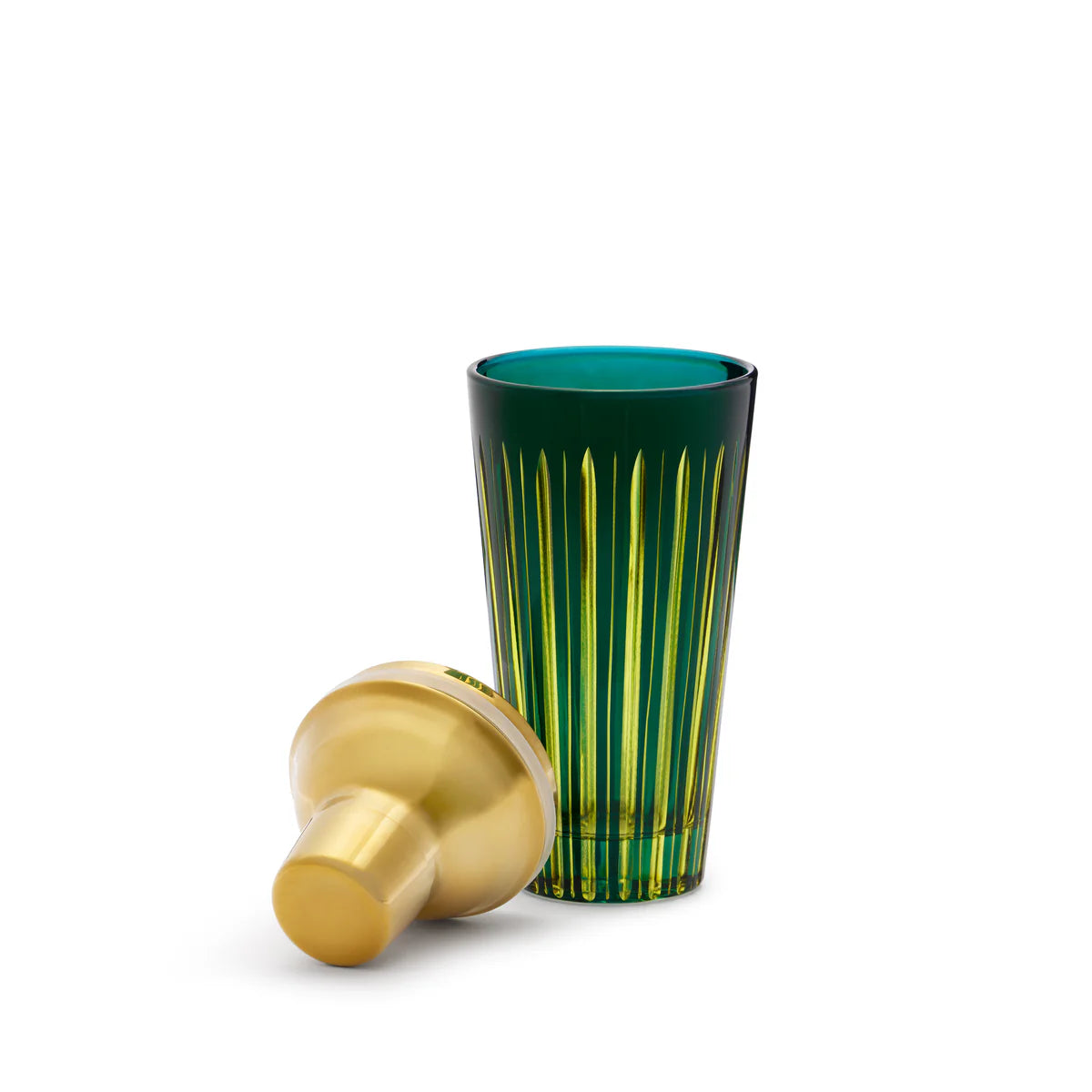 A tall, hand-crafted green glassware with vertical yellow stripes stands upright beside a gold Prism Cocktail Shaker lid by L’Objet, both displayed against a plain white background.