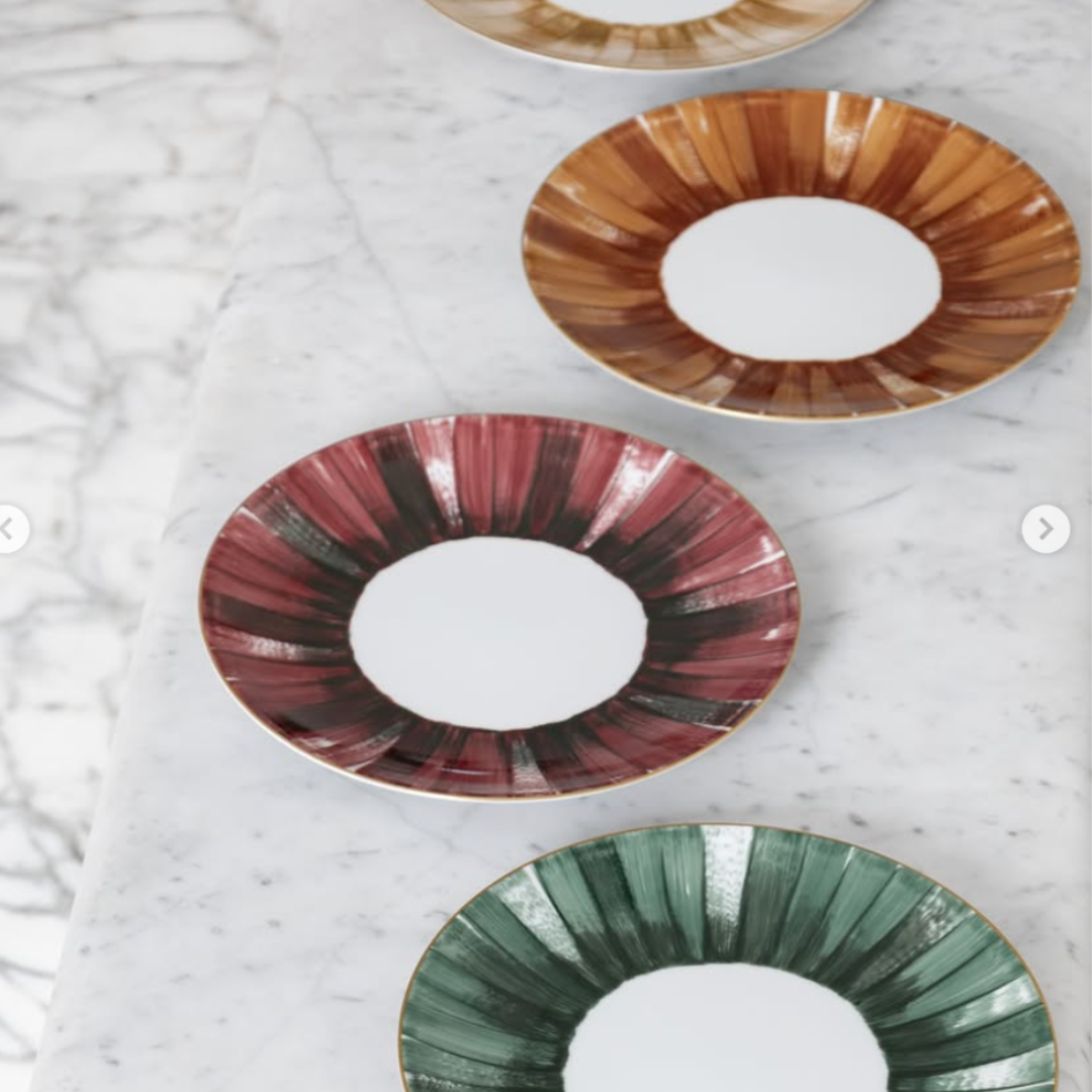 Three Marie Daage Panache plates by Marie Daâge, crafted from hand-painted porcelain with brushstroke designs in rust, gold, and green tones, are artfully arranged on a marble surface.