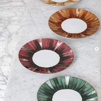 Three Marie Daage Panache plates by Marie Daâge, crafted from hand-painted porcelain with brushstroke designs in rust, gold, and green tones, are artfully arranged on a marble surface.
