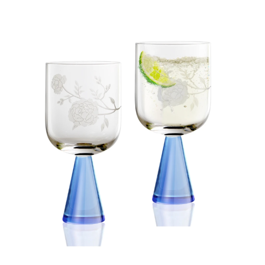 The Current Home Peony Goblet Set of 2 features handcrafted goblets with floral etchings and blue cone-shaped bases; one empty, the other filled with a fizzy drink and lime slices—a charming glassware duo.