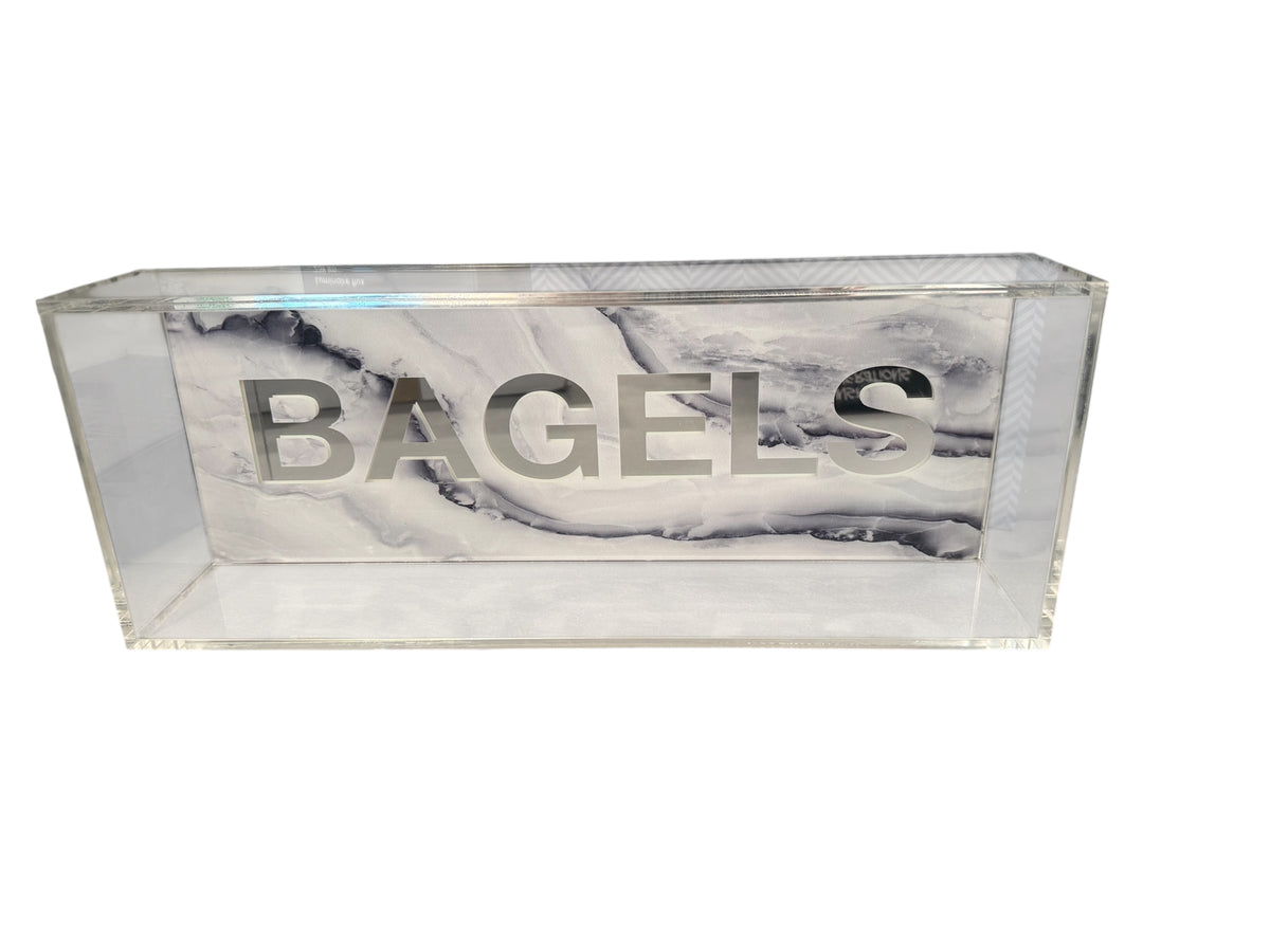 The Eye Candy Bagel Tray is a rectangular, food-safe acrylic tray featuring "BAGELS" in large silver letters on the front, set against a white and silver marble-effect acrylic background.