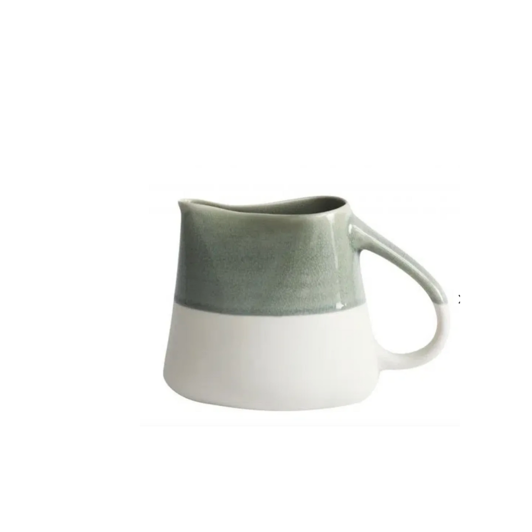 The Maguelone Cachemire Dinnerware by Jars - Rosenthal is a ceramic pitcher with a glossy light green top and matte white bottom, curved handle, and small spout, highlighting artisanal beauty on a plain white background.