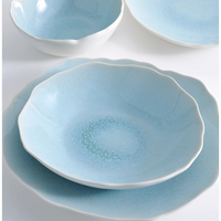The Plume Ocean Blue collection by Jars - Rosenthal features ceramic plates and bowls with scalloped edges and a subtle textured pattern, highlighting artisanal craftsmanship, beautifully displayed on a white surface.