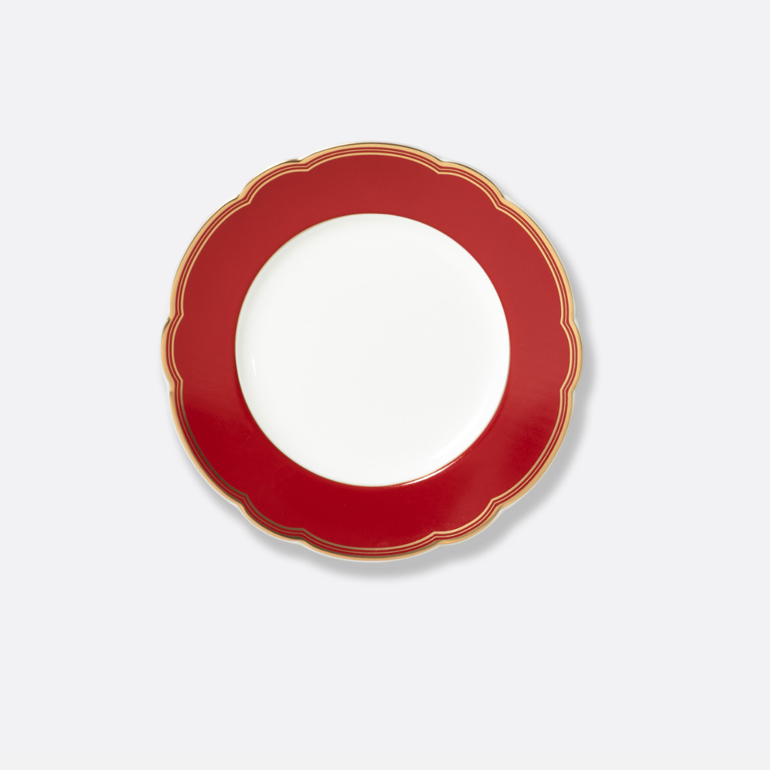 The Bernardaud Pompadour plate, a round white dish with a wide red scalloped and gold-trimmed border, is showcased against a plain light gray background.