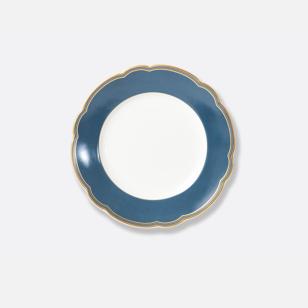 A round white Bernardaud "Pompadour" plate with a wide dark blue border and scalloped gold edge, set against a light gray background—an elegant dinnerware piece from Limoges, France.