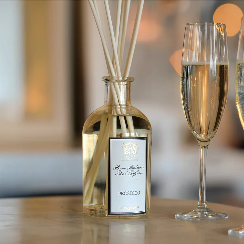 A glass of sparkling prosecco sits beside the Antica Farmacista Prosecco Diffuser by Harper on a marble surface, filling the air with an elegant home fragrance against a softly blurred background.