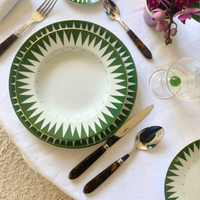 A table setting with Molecot's Punk Dinnerware Green plate on a white cloth, dark-handled cutlery, a glass holding a green marble, and a small arrangement of purple flowers.