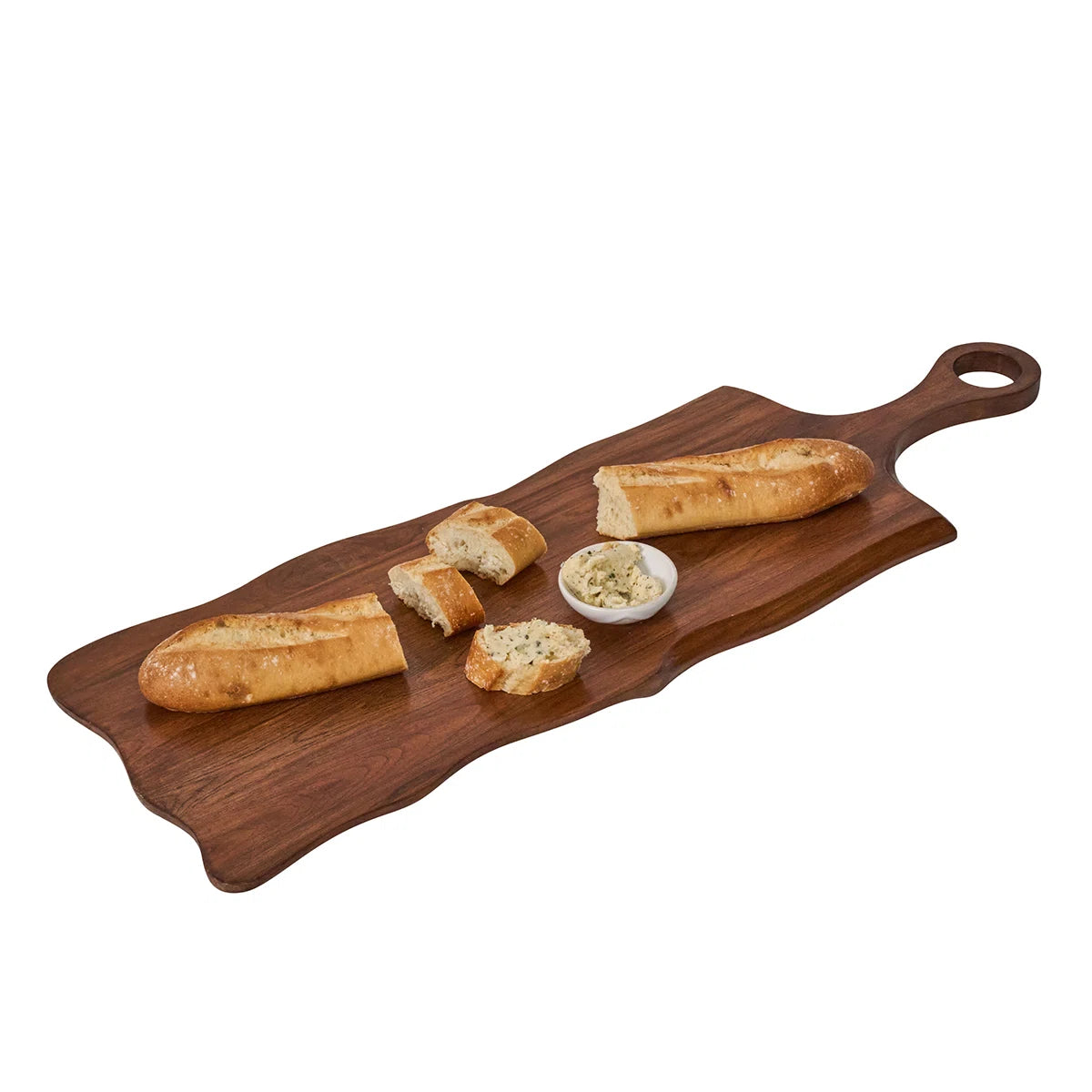 The Juliska Puro Long Serving Board Teak, crafted from solid teak wood, elegantly displays a whole baguette, sliced pieces, and a small bowl of herb butter or dip placed in the center. This artisanal serving board adds warmth and sophistication to any table setting.