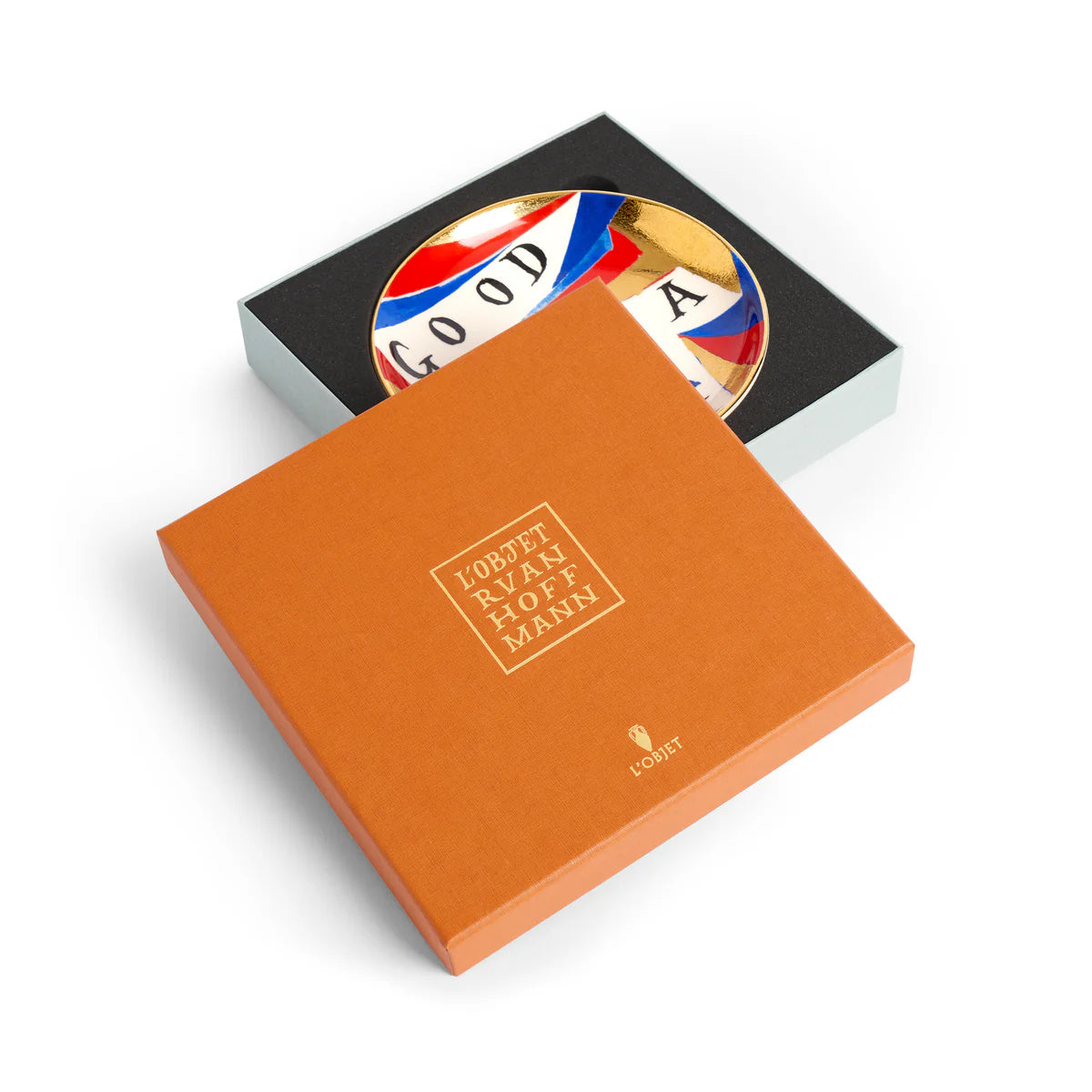 The Good/ - Bad Idea Plate by Ruan Hoffmann for L’Objet, featuring colorful patterns and the word GOOD, is partially revealed in an open orange L’Objet gift box with gold lettering.