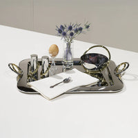A polished stainless steel tray holds a vase with purple flowers, Anna New York Ring Salt & Pepper Shaker Set, an egg in a cup, a napkin with a spoon, and a bowl with brass handle on a white surface.
