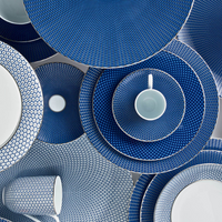 A flat lay of Raynaud Tresor Dinnerware Blue shows blue and white plates and cups with geometric dot and grid patterns, highlighting the collection’s formal elegance.