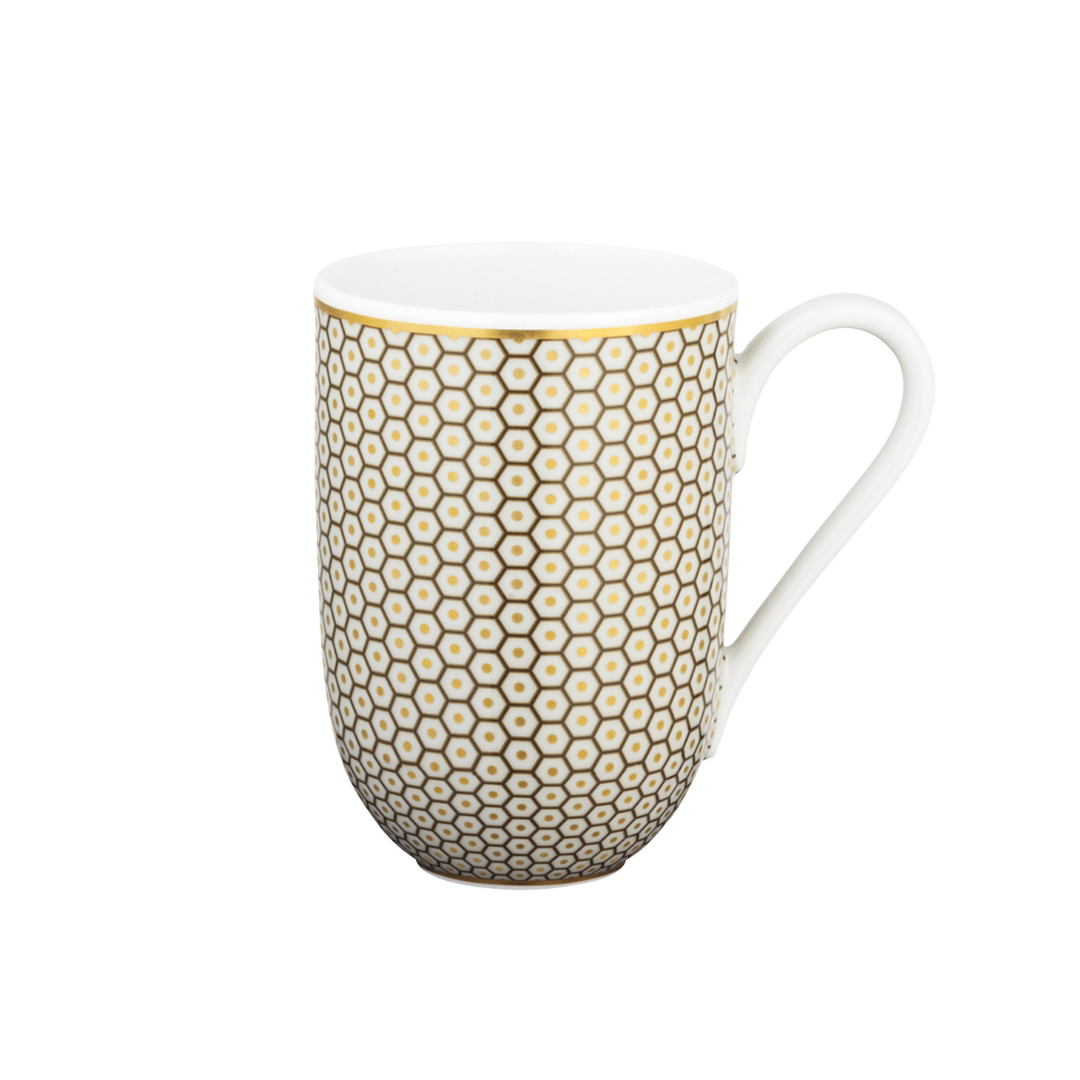 The Tresor Dinnerware Brown by Raynaud is a white ceramic mug with a curved handle, featuring a repeating gold hexagon and dot pattern inspired by Raynaud porcelain, set on a plain white background.