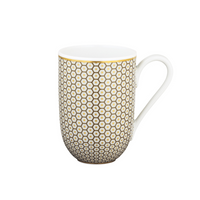 The Tresor Dinnerware Brown by Raynaud is a white ceramic mug with a curved handle, featuring a repeating gold hexagon and dot pattern inspired by Raynaud porcelain, set on a plain white background.