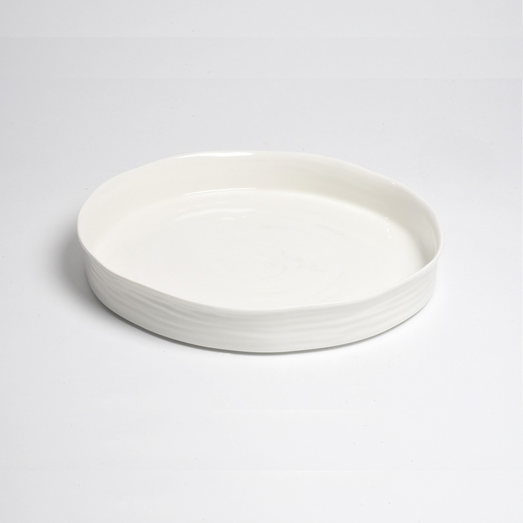 The Le Blanc Round Platter by PAMPA BAY is a shallow white ceramic serving platter with a slightly uneven rim, shown on a plain white background.