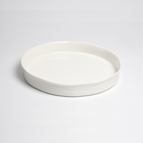 The Le Blanc Round Platter by PAMPA BAY is a shallow white ceramic serving platter with a slightly uneven rim, shown on a plain white background.