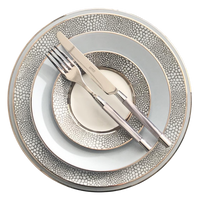 Four stacked Makassar Gray & Platinum dinner plates by Royal Limoges/Bia Cordon Bleu, crafted in France from fine Limoges porcelain with a gray and white pattern; a metallic fork and knife rest diagonally on top.