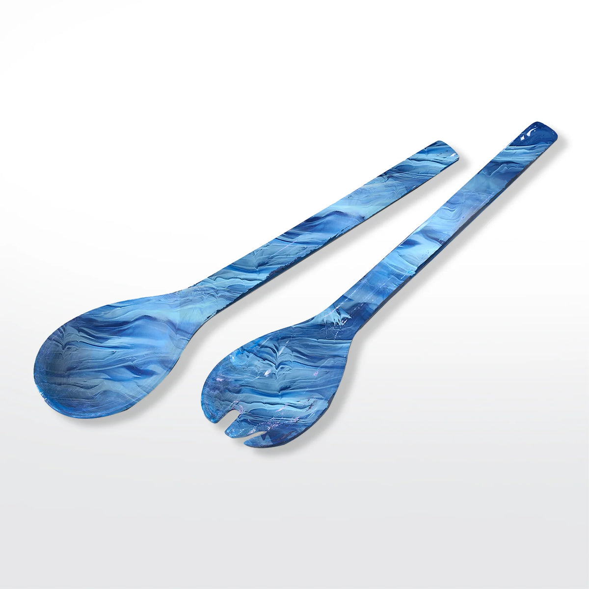Nashi Home's Swirl Resin Colored Everyday Salad Servers in Denim—one spoon and one fork—feature a bold blue marbled look and are crafted from BPA-free resin, shown side by side on a white background for safe, stylish serving.