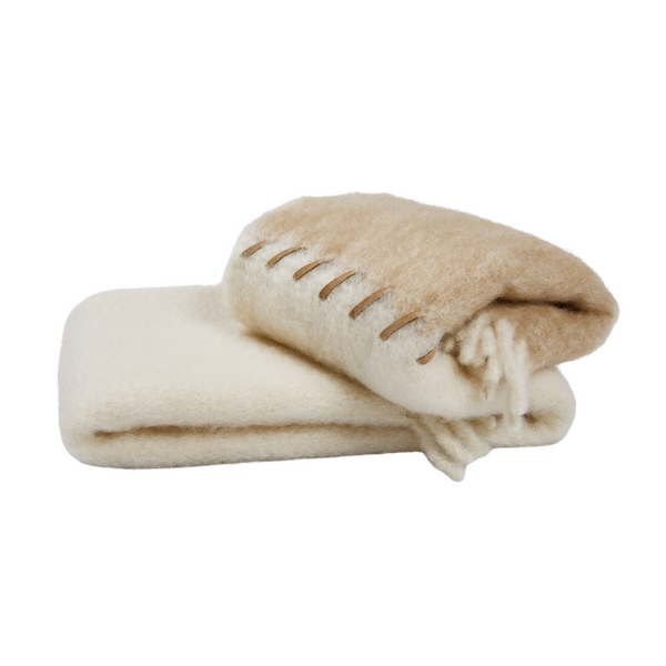 Two folded Mantas Ezcaray Stitching Throw blankets—one beige luxury throw with stitched edging atop a plain cream one—isolated on a white background.