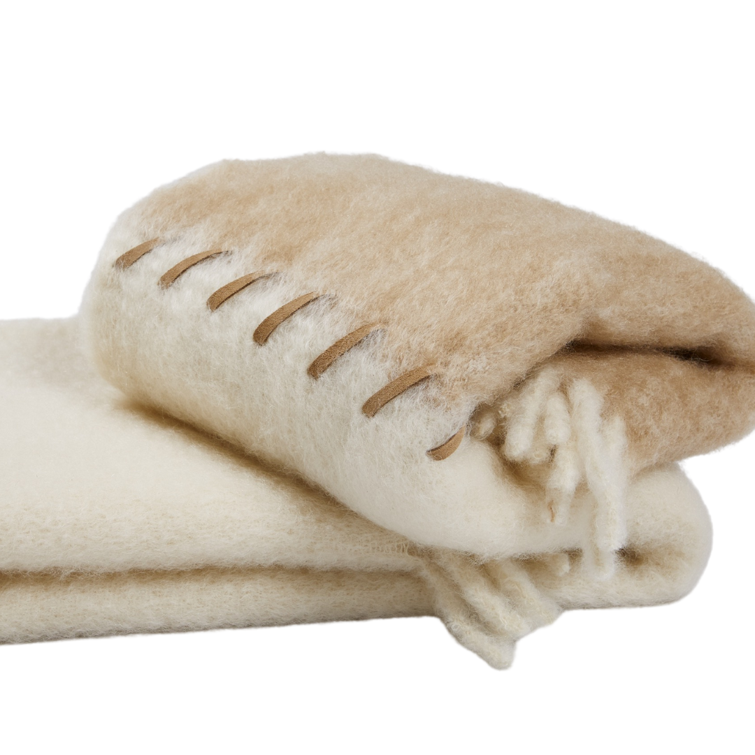 The Mantas Ezcaray Stitching Throw is a handmade, folded mohair blanket in beige and cream with bold brown edge stitching and soft tassels at one end.