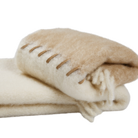 The Mantas Ezcaray Stitching Throw is a handmade, folded mohair blanket in beige and cream with bold brown edge stitching and soft tassels at one end.