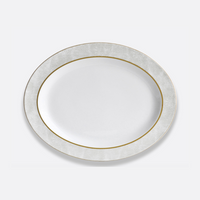 The Bernardaud Sauvage Gold Dinnerware features a white oval Limoges porcelain plate with a textured, light gray and gold snake skin-inspired rim on a plain light background.