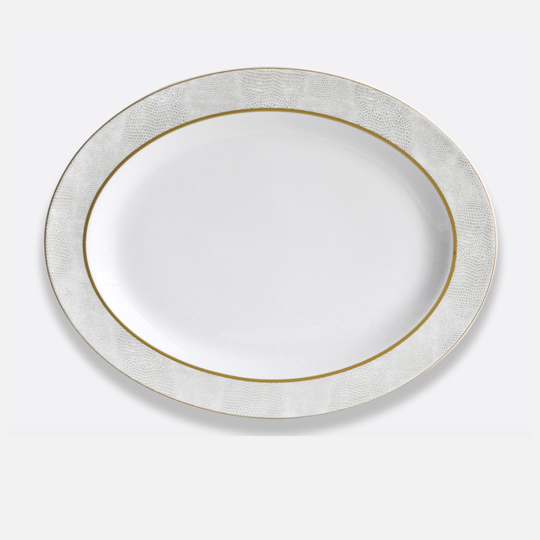 The Bernardaud Sauvage Gold Dinnerware is a white, round Limoges porcelain plate featuring a textured snake skin embossed rim and a fine gold band, displayed on a plain light background.