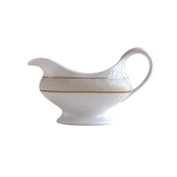 The Bernardaud Sauvage Gold Dinnerware gravy boat is crafted from white Limoges porcelain, features an embossed snake skin pattern, a curved handle and spout, and a thin gold accent band around the middle.