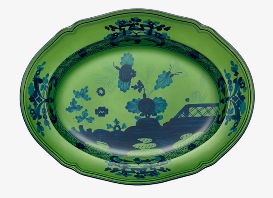 The Ginori 1735 Oriente Italiano Dinnerware Malachite is an oval ceramic platter with a green background and dark blue floral and landscape motifs, including trees and a bridge—an eye-catching piece of Italian tableware.