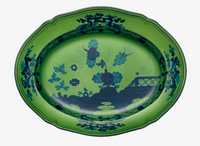 The Ginori 1735 Oriente Italiano Dinnerware Malachite is an oval ceramic platter with a green background and dark blue floral and landscape motifs, including trees and a bridge—an eye-catching piece of Italian tableware.