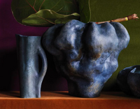 The Timna Vase Short by L'Objet, featuring a unique hand-glazed blue porcelain design with an irregular surface, sits beside a tall blue pitcher on an orange surface, accented by green leaves and a green and purple background.