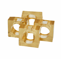 The Tizo Lucite Cube Napkin Ring Set of 4 features gold-colored, square acrylic rings with large circular cutouts—elegant accents to elevate your modern table decor.