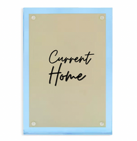 The Tizo Lucite Magnetic Frame Blue features a rectangular gold-colored acrylic sign with rounded corners, light blue edges, and "Current Home" in black cursive at the center, held by four round magnetic fixtures.