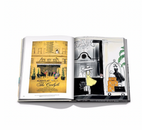 An open book, "The Carlyle" by Assouline, displays an illustration of The Carlyle Hotel entrance on the left and a woman in yellow speaking to a concierge by a luggage cart in its iconic Upper East Side lobby on the right.