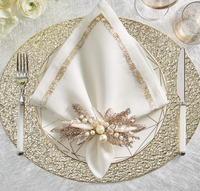 The Kim Seybert Impression White & Gold Napkin Set of 4 features elegant white linen with an embroidered border and gold metallic stitching, perfect for a chic table setting when paired with decorative plates and sparkling gold accents.