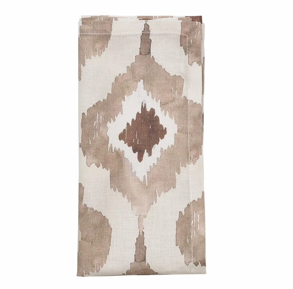 The Kim Seybert Watercolor Ikat Napkin Taupe Set of 4 features a folded beige linen napkin with a geometric diamond pattern in brown and taupe accents, displayed on a white background.