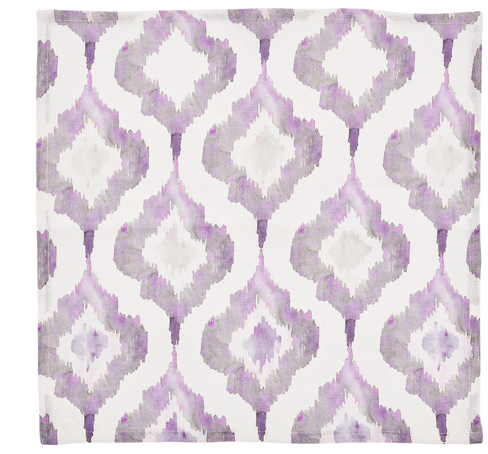 The Kim Seybert Watercolor Ikat Napkin Lilac & Grey Set of 4 features folded white linen napkins with a repeating lilac and grey watercolor-style Ikat pattern.