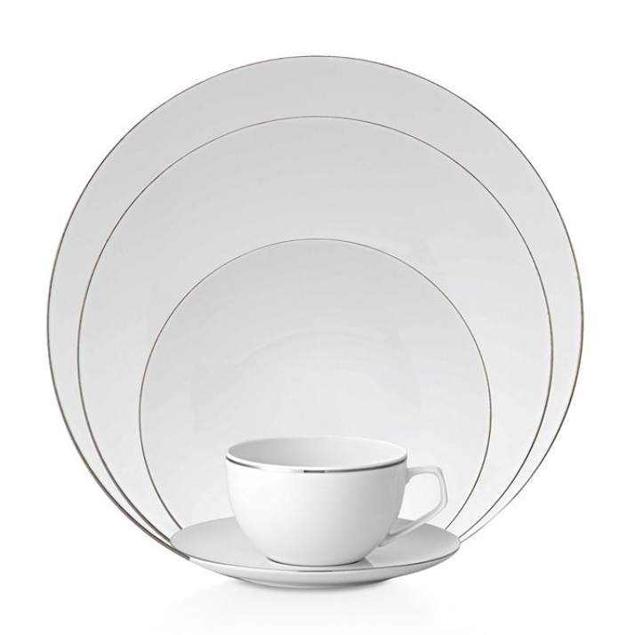 A Rosenthal TAC 02 Platinum Filet teacup and saucer sit before stacked white dinnerware plates, each edged with a simple silver rim.