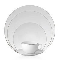 A Rosenthal TAC 02 Platinum Filet teacup and saucer sit before stacked white dinnerware plates, each edged with a simple silver rim.