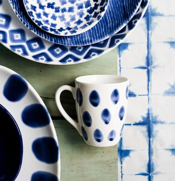 Vietri’s Santorini Mug Assorted Set of 4, featuring geometric and dotted blue and white patterns, displayed on a wooden table with a blue tie-dye napkin.