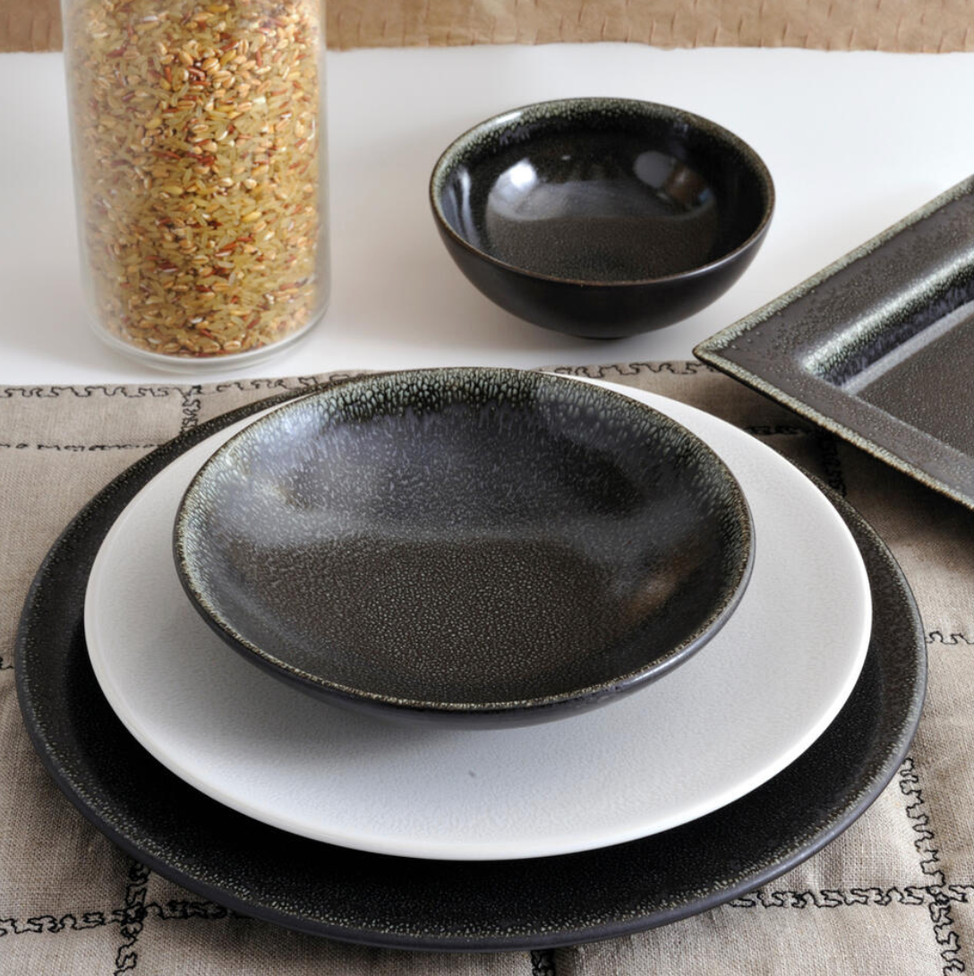 The Tourron Dinnerware Celeste by Jars - Rosenthal features two plates, a shallow bowl, and a small bowl in black and white tones. These elegant glazed stoneware pieces are dishwasher safe and beautifully displayed beside a jar of mixed rice.