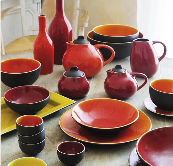 The Tourron Dinnerware Cerise by Jars - Rosenthal features vibrant red, orange, and yellow ceramic bowls, cups, teapots, and pitchers with beautiful glazes, stylishly arranged for an elegant tableware display.
