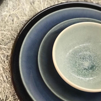 A close-up of three nested Tourron Dinnerware Celeste stoneware dishes by Jars - Rosenthal in varied sizes and blue-gray shades, arranged on a surface covered with white shredded material.