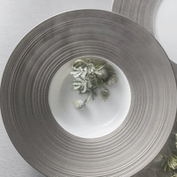 The JL Coquet Hemisphere Dinnerware Platinum plate features white Limoges porcelain with a wide, textured platinum rim, perfect for showcasing elegant touches like silvery-green sprigs and frosted berries on a sophisticated table setting.