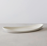 The Barre Serving Platter - Alabaster by Simon Pearce is a sleek, elongated white ceramic piece with gently curved edges, shown on a light gray surface against a minimalist background.