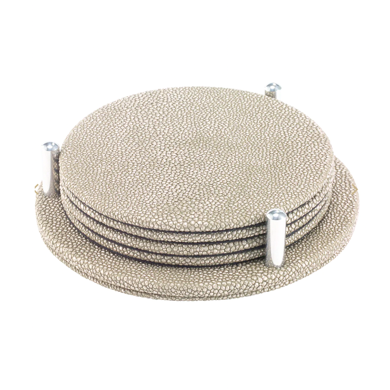 The Bodrum Stingray Coaster Set of 4 features textured, round beige coasters with a subtle metallic finish, stacked neatly in a matching holder with three vertical pegs for secure, stylish storage.