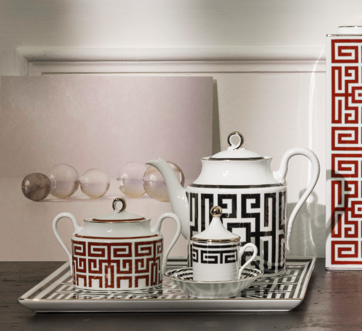 The Ginori 1735 Labirinto Dinnerware Nero is a decorative tea set with a Greek key pattern in black and red on a matching tray, featuring a teapot, sugar bowl, and creamer with geometric design and shiny metallic accents inspired by Gio Ponti.
