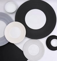 A flat lay of JL Coquet's Hemisphere Dinnerware Bakelite Black plates and bowls, featuring concentric circle designs in black and white tones, arranged overlapping on a white background.
