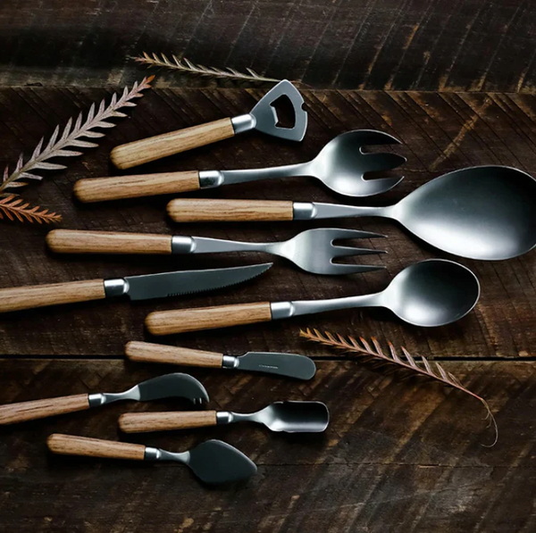 The Vietri Albero Flatware 5 Piece Setting - Oak features stainless steel black and silver utensils with Albero Oak wooden handles, including spoons, forks, a knife, bottle opener, and cheese spreaders.