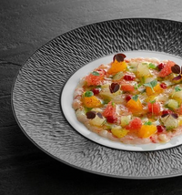 A gourmet dish is artfully presented on the Mineral Irise Dinnerware Dark Grey by Raynaud, with vibrant fruit and herb pieces atop a translucent base, garnished with microgreens for a striking, colorful display.